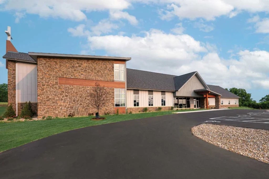 church with gray roof, tan siding, rocky landscaping