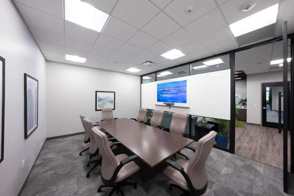 Gray conference room with large table and 8 chairs, plus large video screen wall
