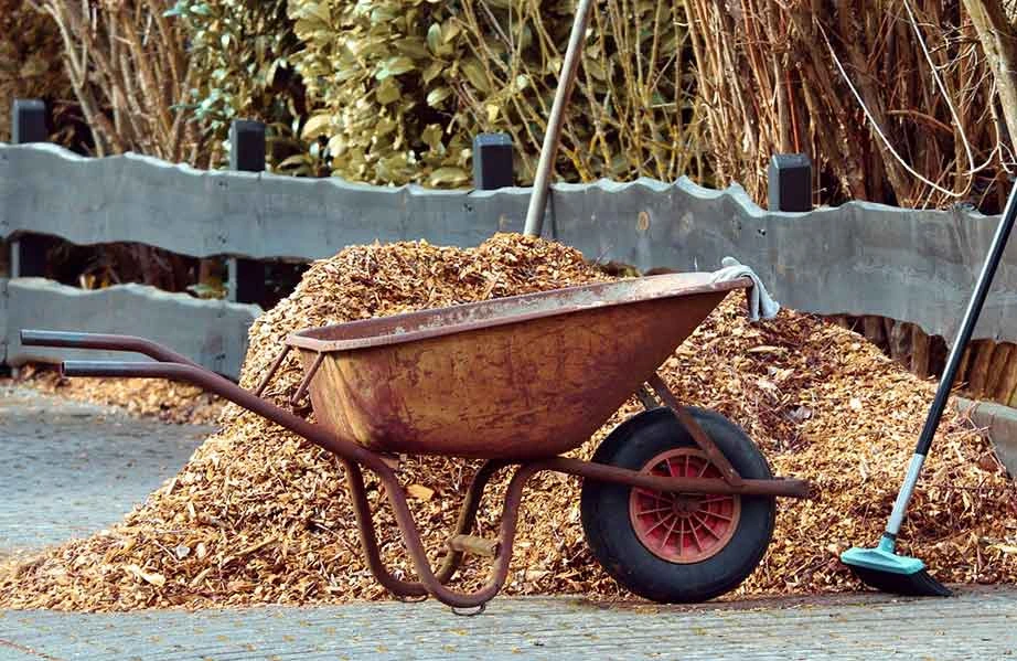 rusty wheelbarrow next to pile of mulch with broom nearby