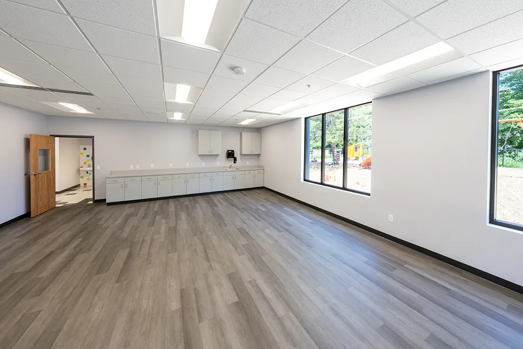 Classroom with white walls, windows, woodgrain floor, cabinets and sink