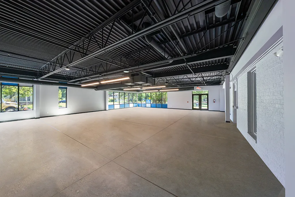 Large interior space with dark ceiling, many windows, cement floor