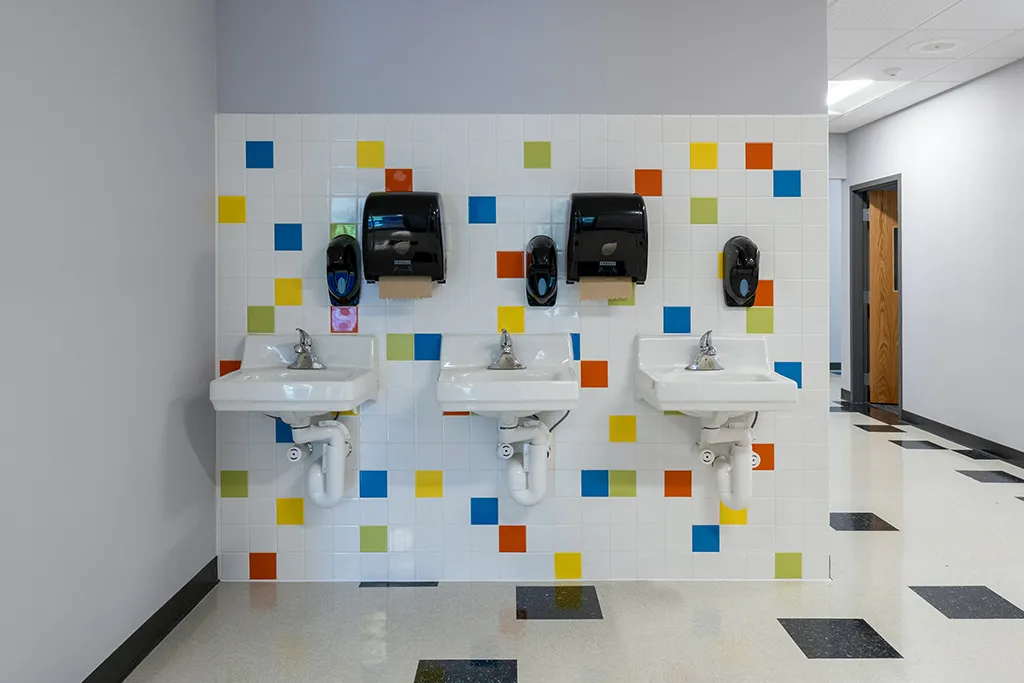 Wall with colorful tile, three sinks, soap dispensers and towel dispensers