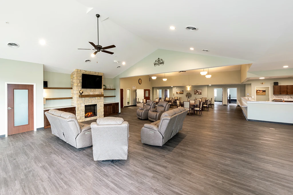 Large room with gray sofas and chairs, stone fireplace, tables, window and ceiling fan