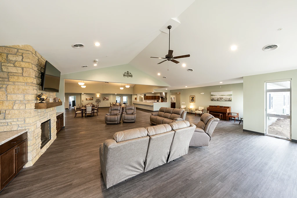 Large room with gray sofas and chairs, stone fireplace, tables, window and ceiling fan