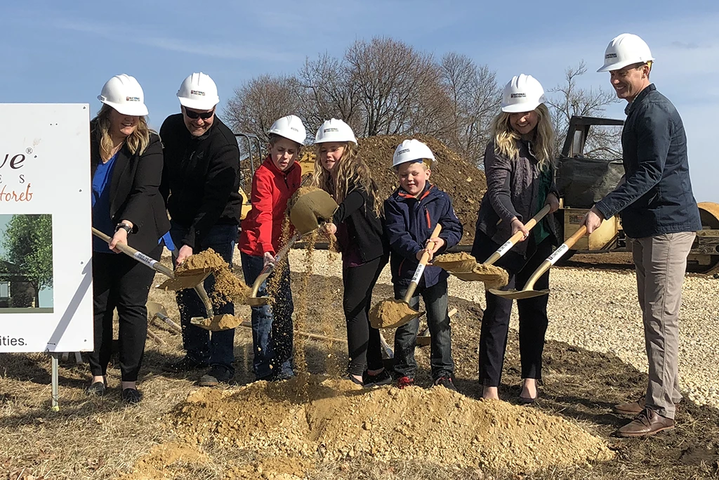 seven people in hard hats scooping dirt with shovels
