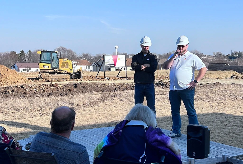 two men in hard hats address spectators at a groundbreaking event