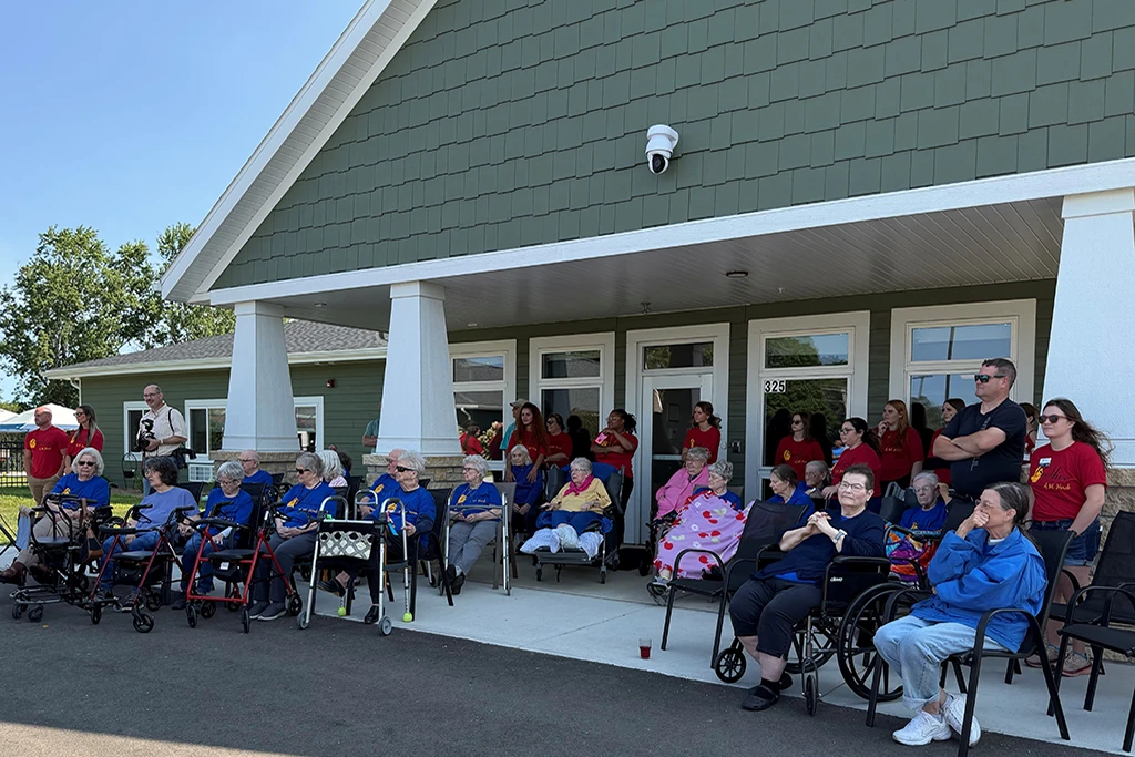 Residents gathered outside green and white residential facility for ribbon cutting celebration