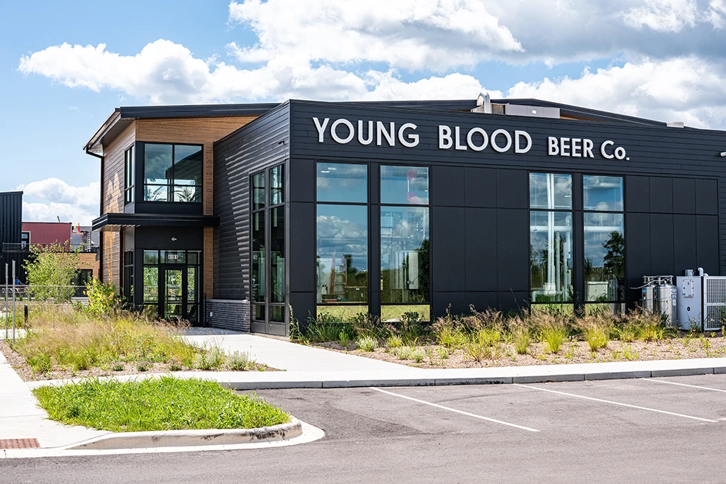 Large gray brewery with large windows and attached restaurant with brown siding