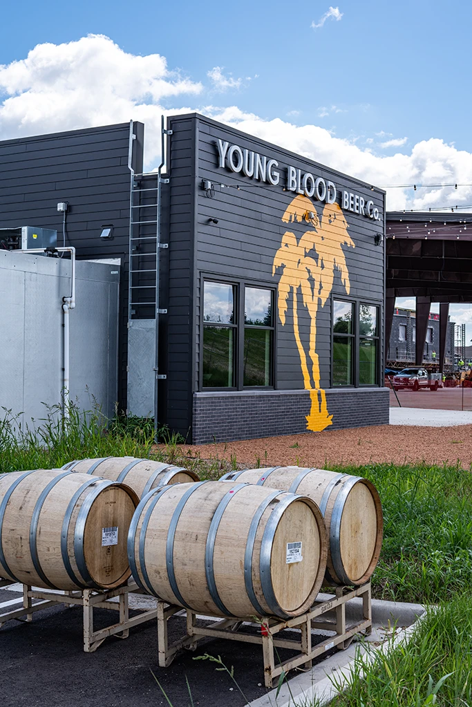 Exterior of building with dark gray siding, yellow palm trees painted on wall, and wood barrels