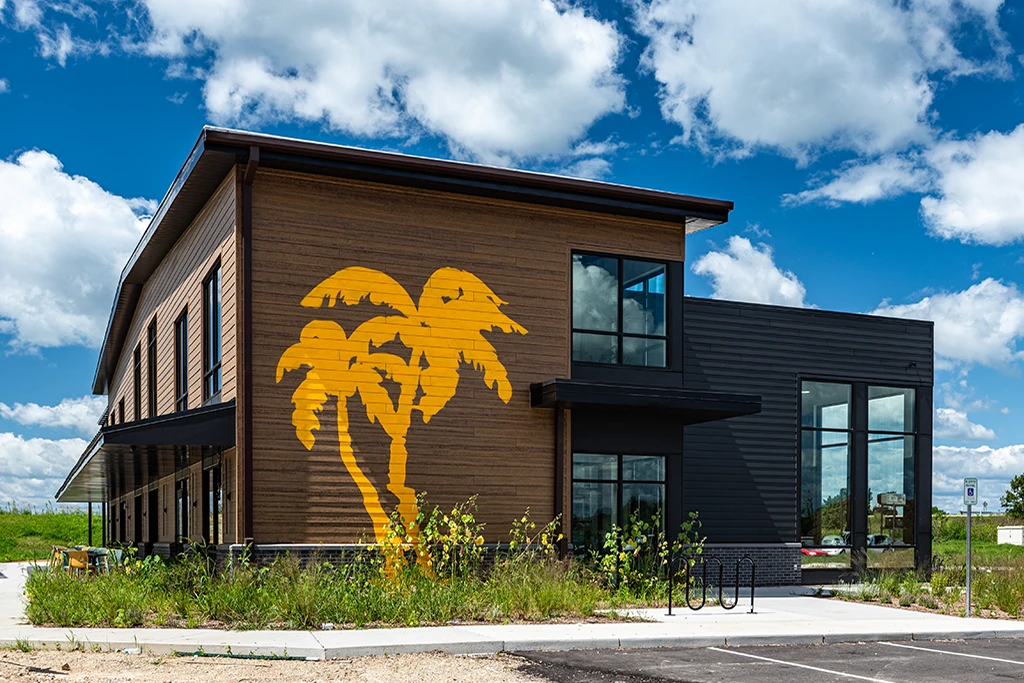 Building with brown and gray siding, large windows, and two yellow palm trees painted on wall
