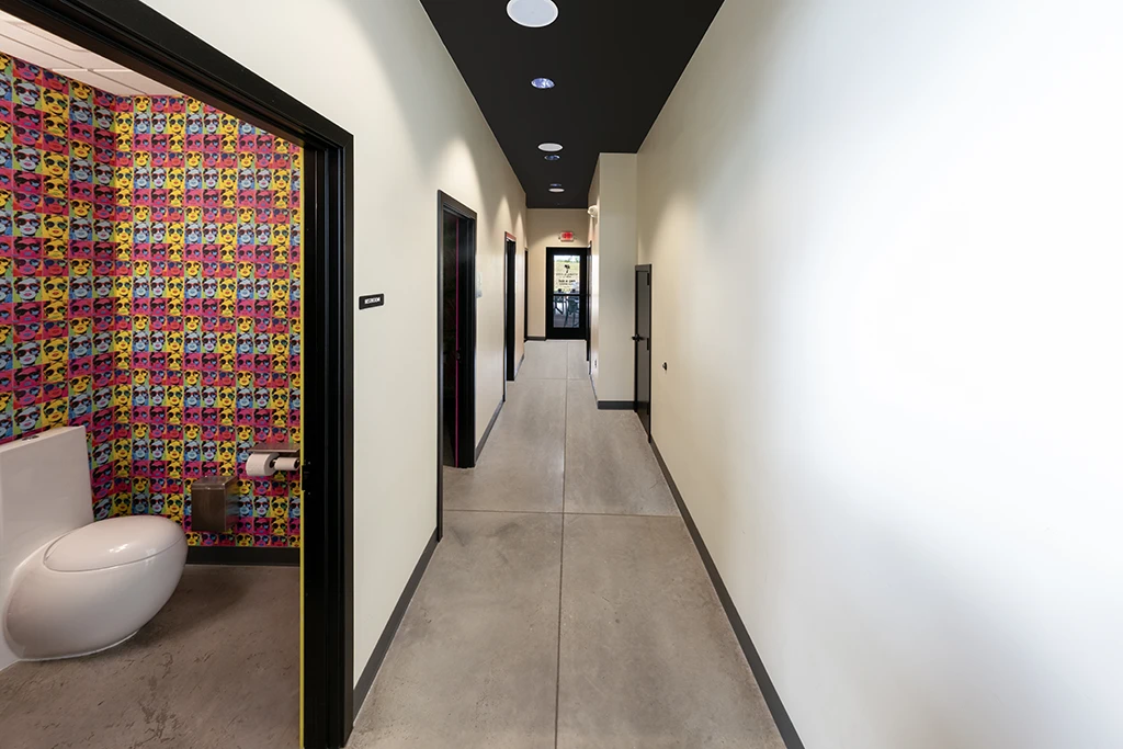 White hallway with black trim and view into bathroom with colorful wallpaper