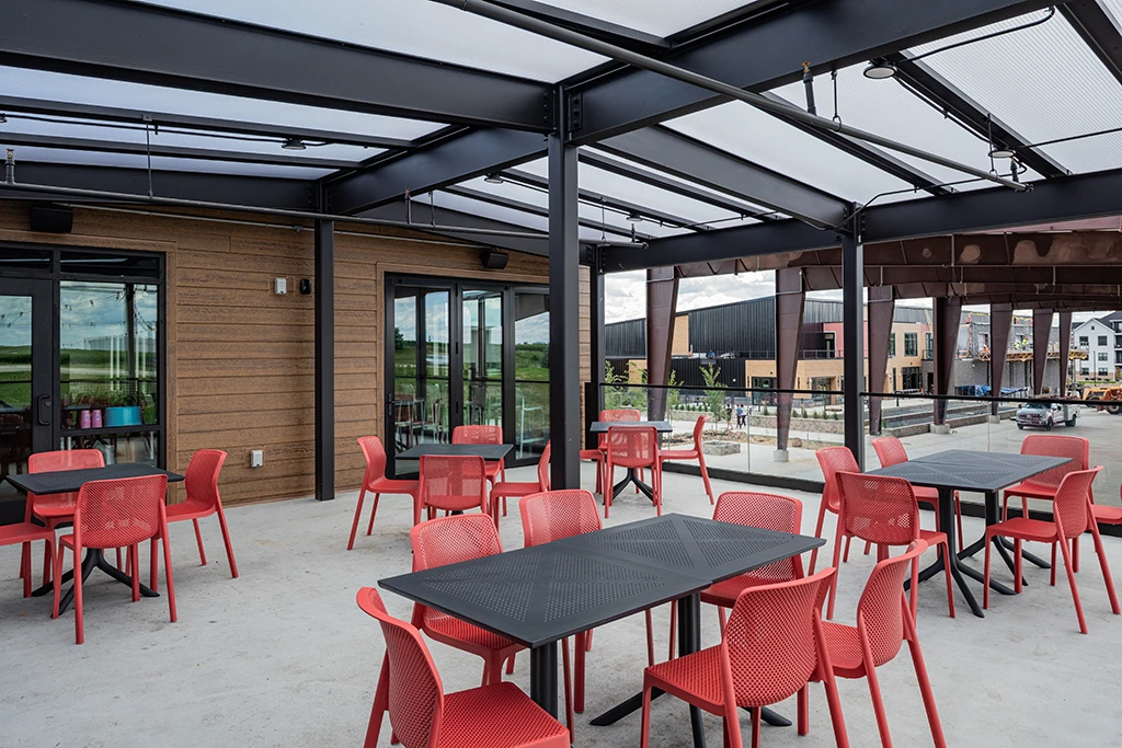 Rooftop patio with brown building in background and translucent roof, red chairs and tables
