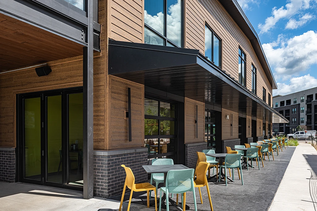 Brown building exterior with long sidewalk and colorful chairs