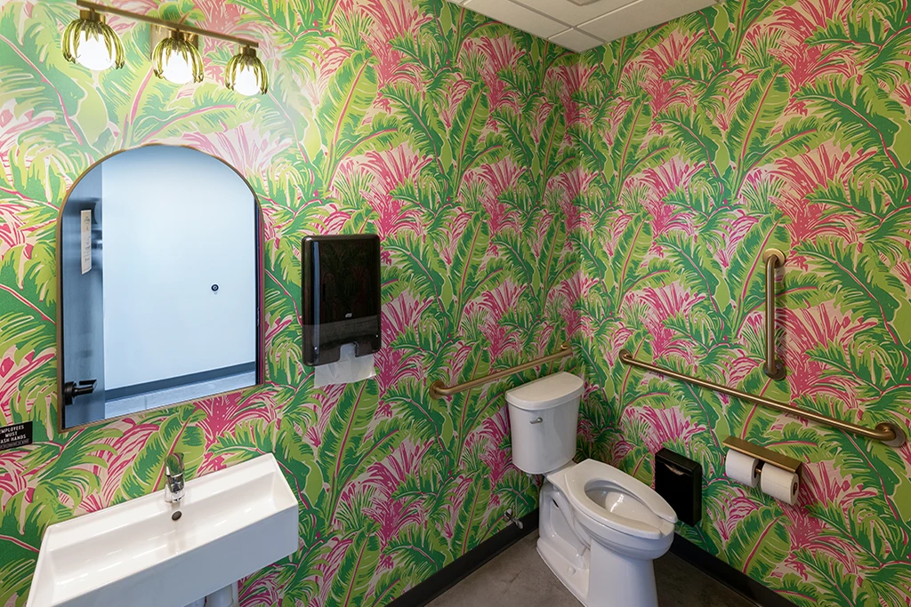 bathroom with toilet, sink, mirror, and colorful tropical wallpaper